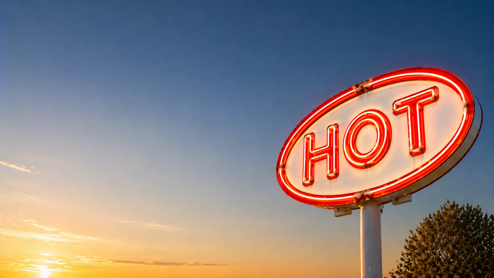 A glowing roadside neon HOT sign against a sunset sky
